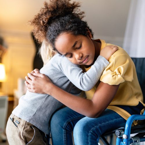 Black little girl with disability in wheelchair hugging with her younger brother